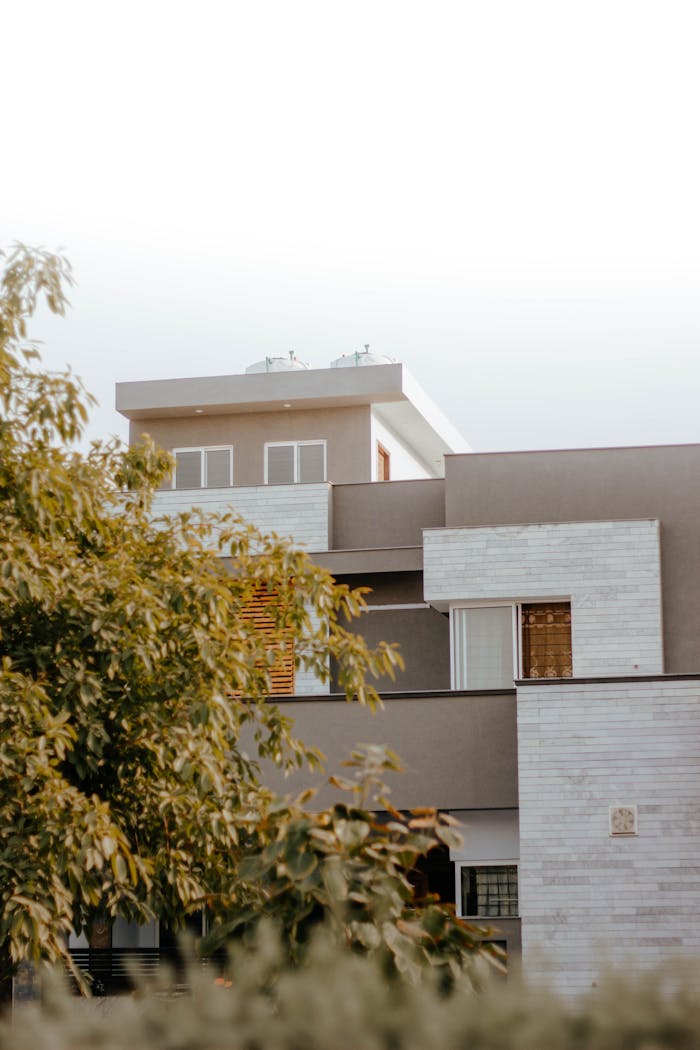 about-02 A modern residential building surrounded by greenery under a clear blue sky.