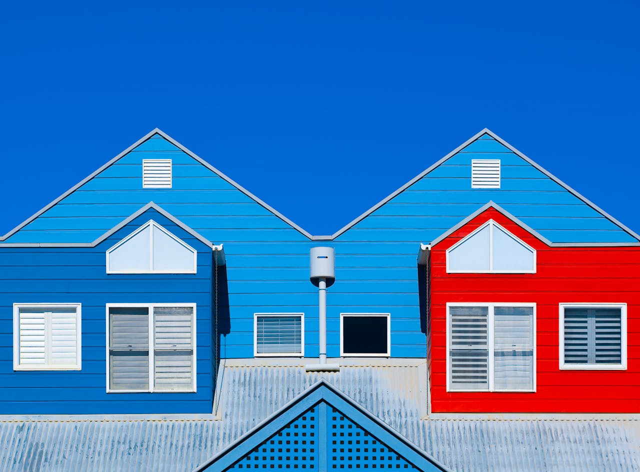 ours-journey Brightly painted house facades in blue and red create a striking contrast against a clear blue sky.