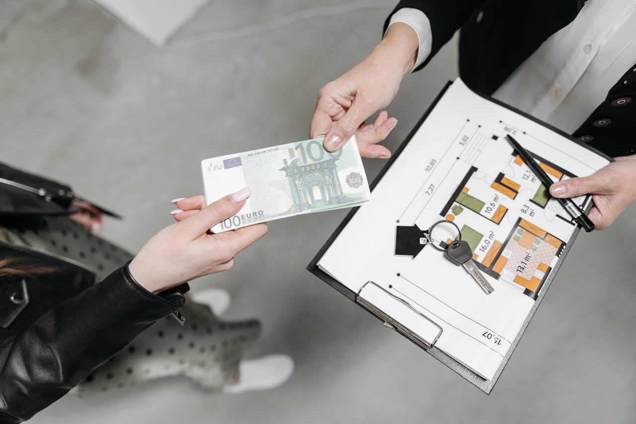 Close-up of a real estate transaction with euro bill, keys, and floor plan.