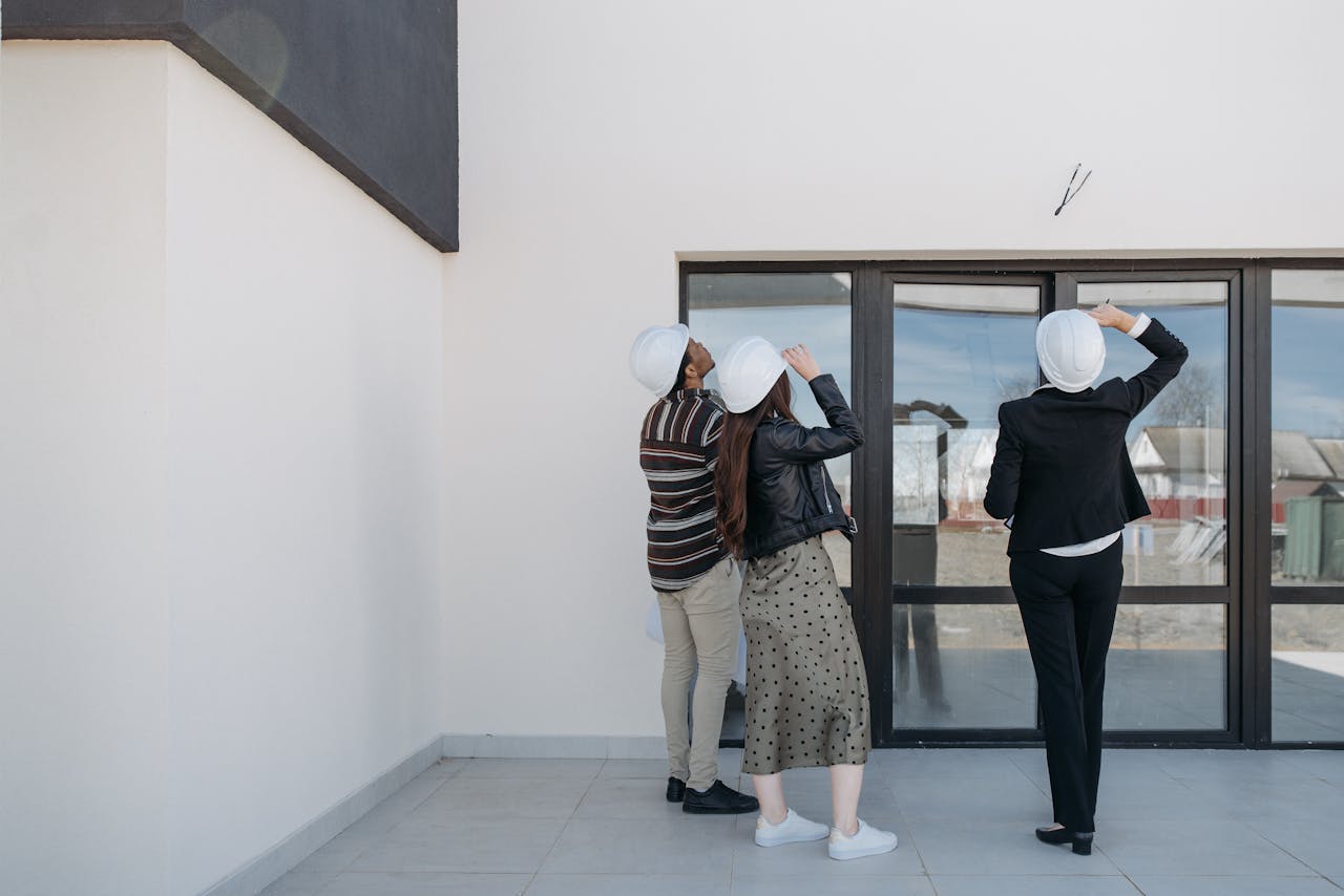 Three architects evaluating exterior building structure, wearing helmets and business attire.